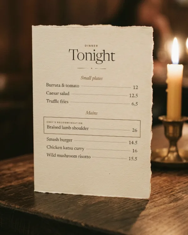 An engineered dinner menu on a candlelit table, with the best-earning dish boxed as chef’s recommendation.